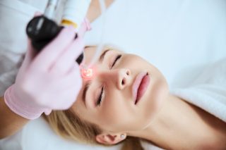 Tranquil female patient lying with closed eyes during the laser treatment in a beauty clinic
