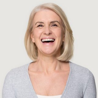 Head shot portrait overjoyed blond middle aged female smiling look at camera laughing feels happy pose isolated on grey studio background, advertise clinic procedure dental care prosthesis for seniors